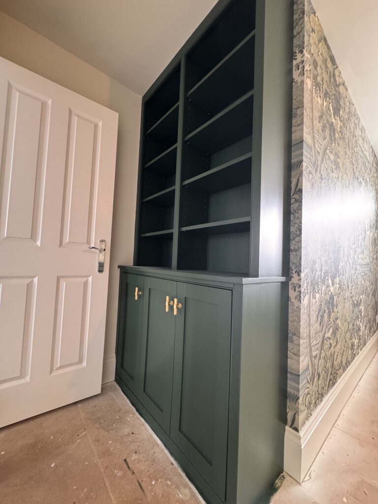 Alcove cupboards and shelving painted deep green beside a mural wall