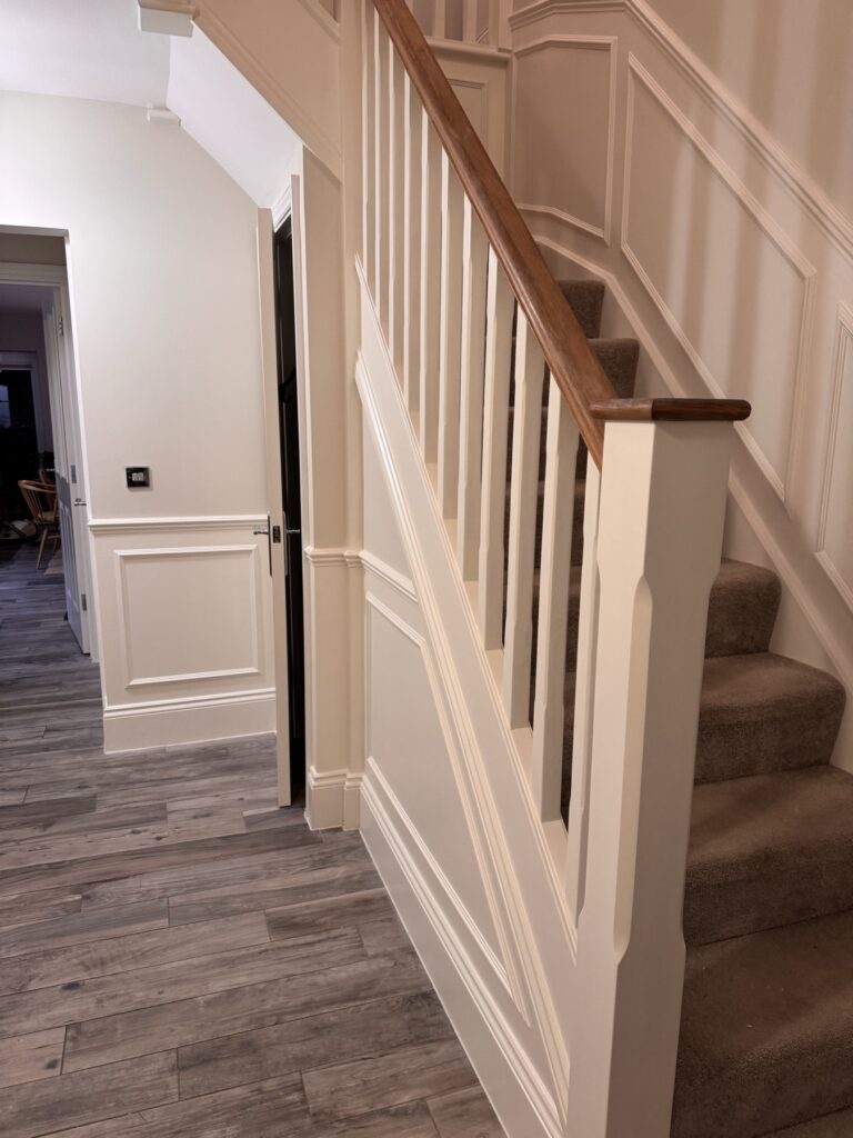 Hallway and staircase with white panelling, spindles and oak handrail
