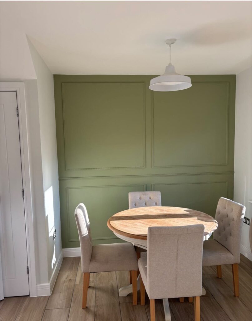 Olive green panelled wall behind a round dining table and chairs